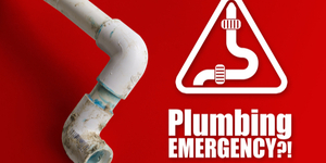 The Phrase "Plumbing Emergency" on a red background next to a broken plastic pipe. Plumbing Emergency concept.