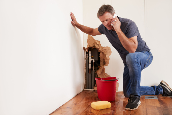 A middle-aged man calling for help after a burst water pipe. Pipe bursting problems concept.