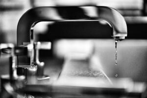 Water drips from a silver faucet: concept, low water pressure in the kitchen sink.