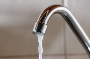 Water trickles slowly from a faucet, shown in a horizontal view: concept, low water pressure in the kitchen sink.