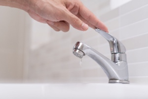 A volunteer turns off running water in the bathroom to conserve water and protect the environment. The concept represents how to save water.