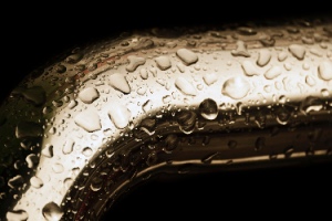 A yellow metal pipe with raindrops isolated on black symbolizes cold water pipe condensation.